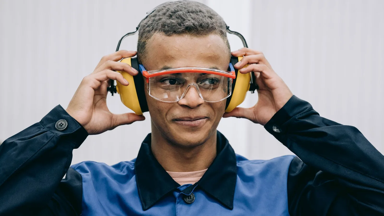 Trabalhador industrial com capacete e aparelho auditivo, ajustando o dispositivo em ambiente de fábrica