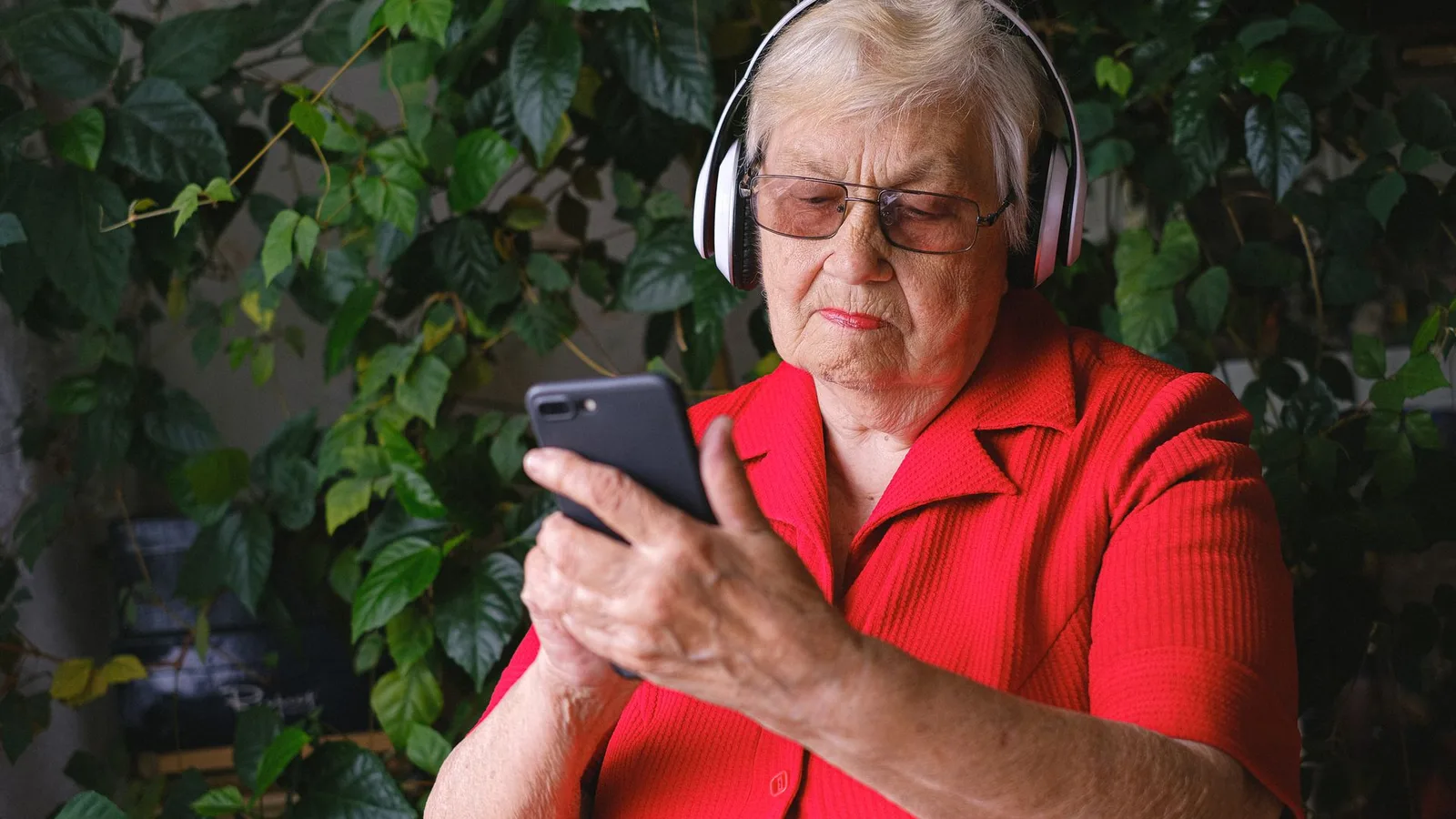 Idosa sorridente segurando celular enquanto ajusta aparelho auditivo moderno no consultório