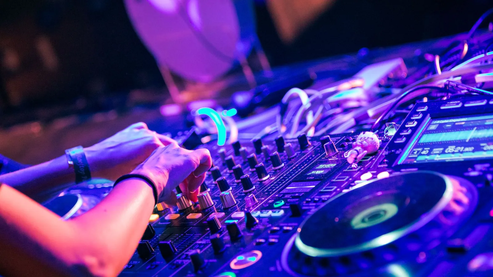 DJ operando mesa de som em ambiente com luzes coloridas