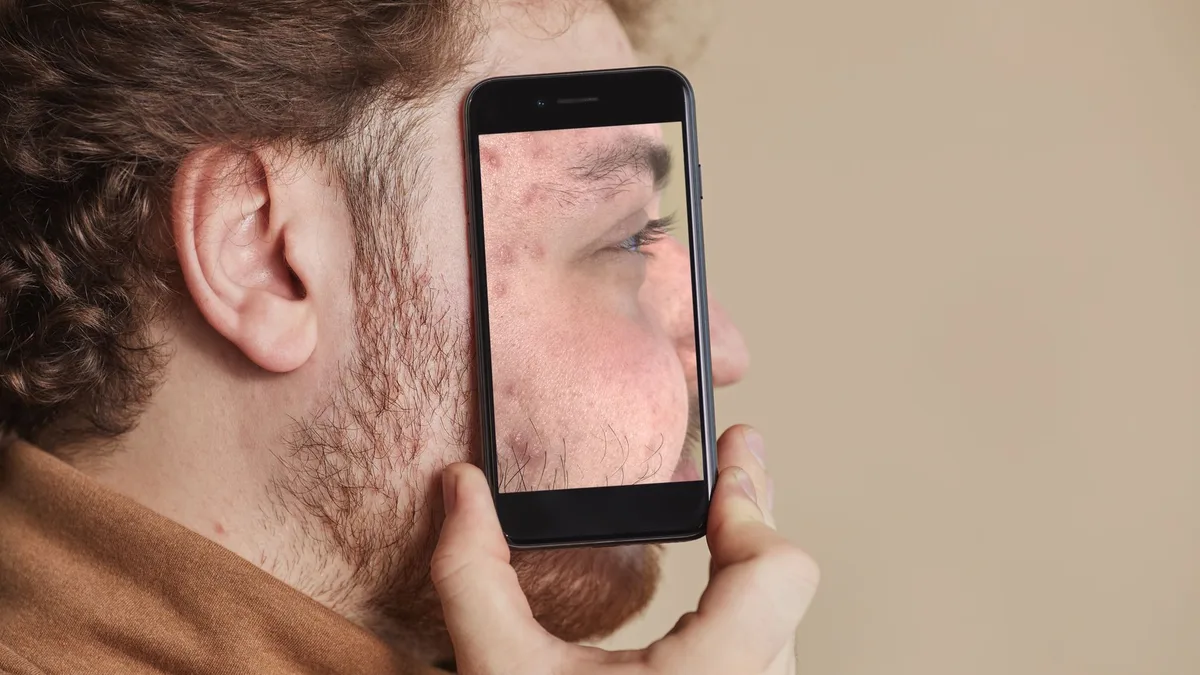 Homem segurando smartphone com reflexo do próprio rosto na tela